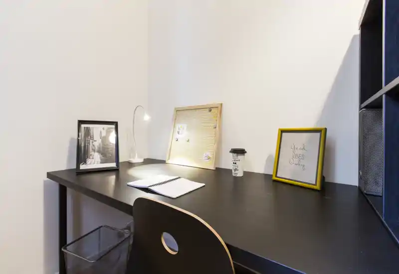 Zona studio ordinata con scrivania nera, lampada da lavoro, stampe incorniciate e bacheca: ideale per lavorare o leggere con concentrazione.