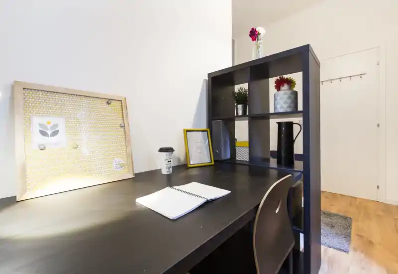 Angolo scrivania luminoso e ben organizzato all'interno della zona giorno — scrivania in legno scuro con scaffalatura aperta, piante e cornici decorative che creano un accogliente angolo studio.