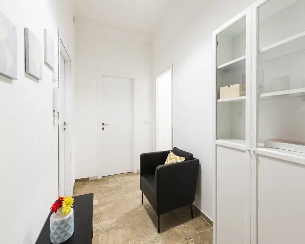 Ingresso luminoso e minimale con una poltrona, armadio a muro e pavimento in pietra neutra — ideale come accogliente foyer.