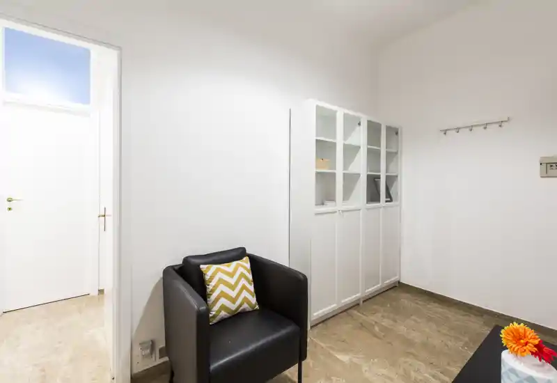 Compact living area with a black armchair, chevron cushion and white storage cabinets; neutral walls and good natural light make it suitable for a small lounge or waiting area.
