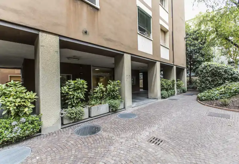 Covered courtyard/entrance with planted containers and a paved brick driveway providing a neat, sheltered approach to the building.