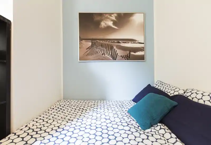 Bright, neatly staged bedroom with patterned bedding, teal accent pillows and a framed seascape above the bed — ideal for a cozy rental listing.