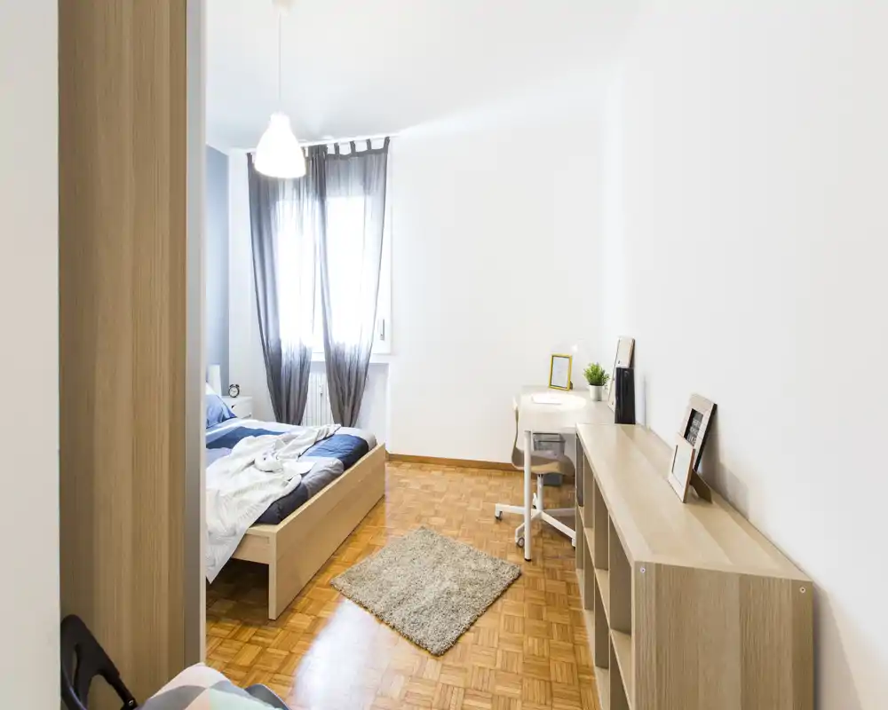 Sunny, modern bedroom with a wooden platform bed, light parquet floor, a small rug and a bright workspace by the window — minimal, well-lit and cozy.