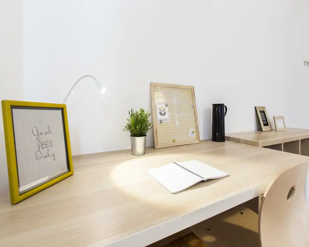 Bright, minimal desk area with light wood surfaces, decorative frames and a small plant — a tidy workspace corner ideal for focused work or study.