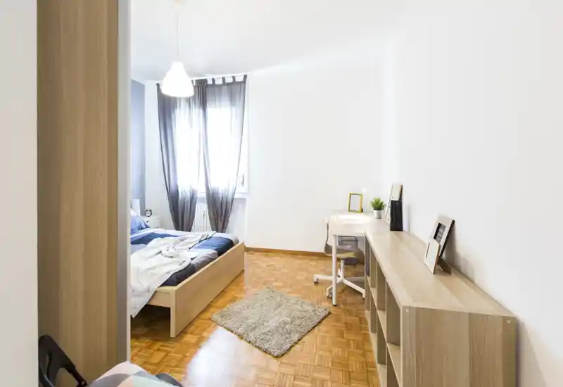 Sunny, modern bedroom with a wooden platform bed, light parquet floor, a small rug and a bright workspace by the window — minimal, well-lit and cozy.
