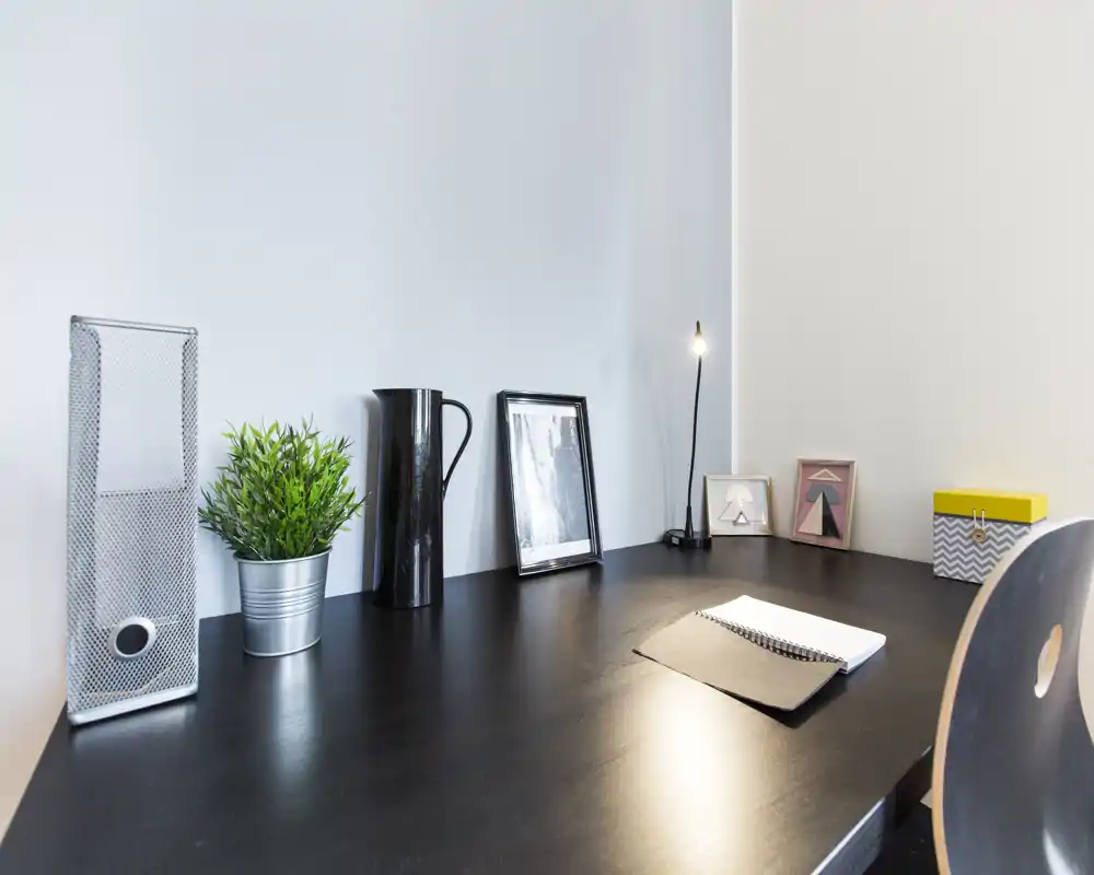 A tidy modern desk area with decorative items — potted plant, framed photos, a slim lamp and a notebook on a dark wooden surface, ideal for a compact workspace.