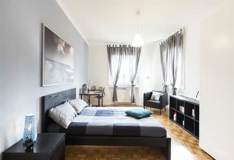 Bright, modern bedroom with a large double bed, wooden parquet floor, desk by the window and cozy armchair — ideal for a comfortable stay.