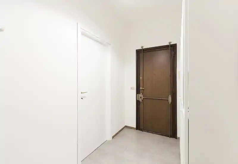 Simple, well-lit entrance with a sturdy wooden front door and clean white walls — ideal as an uncluttered foyer space.