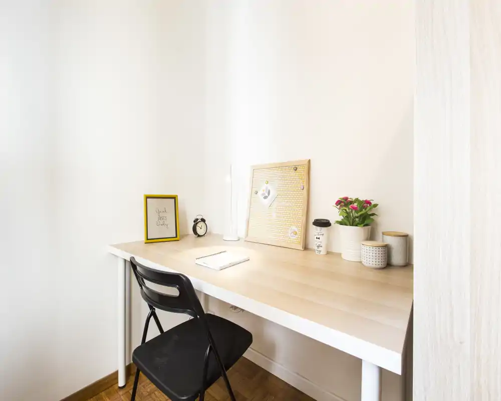 Bright, tidy workspace set against a light wall — a simple desk with a chair, lamp, pinboard and small plants, ideal for remote work or study.