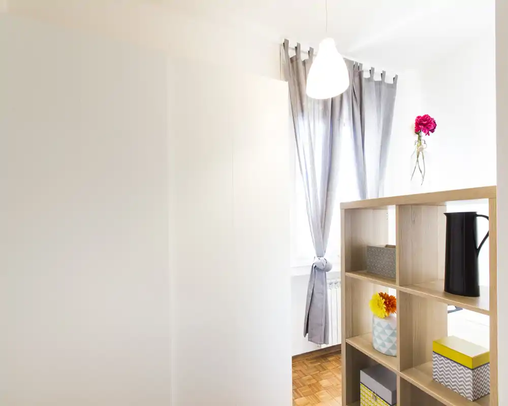 Bright, modern living area with a wooden cube shelf, decorative boxes and a window with grey curtains letting in natural light.