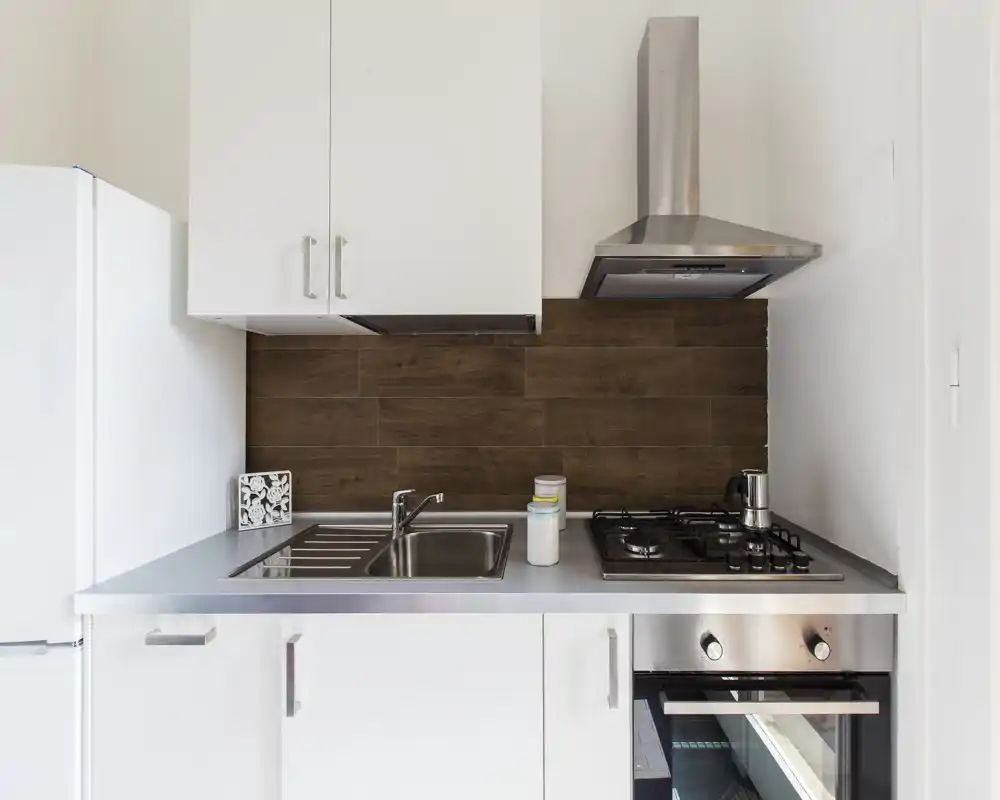 Compact modern kitchenette with stainless steel sink, gas hob, oven and wood-effect backsplash — bright, clean and practical for short-term stays.