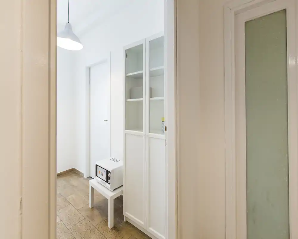 Small, bright entrance or corridor with white cabinetry, a pendant lamp and a tiled floor; a compact appliance sits on a stool by the cabinet.