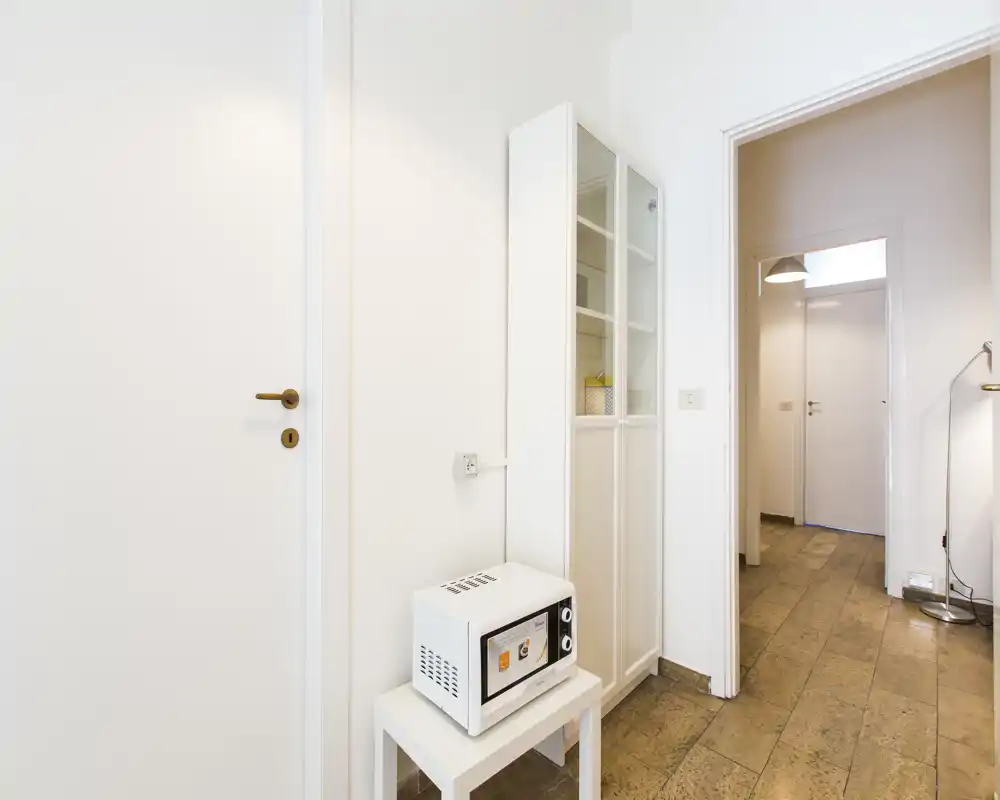 Compact entrance/hallway area with light walls, tiled floor and a small cabinet; clean, bright passage leading to inner rooms.
