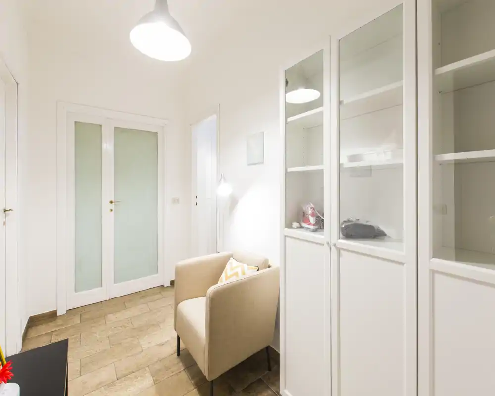Small, bright seating area with a comfortable armchair, floor lamp and built-in cabinets — ideal as a cozy reading nook or entrance sitting spot.