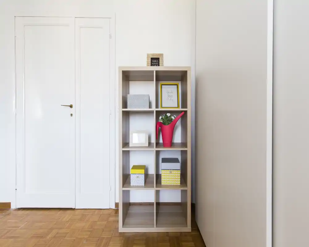Entrada luminosa y minimalista con una estantería de cubos de madera y cajas decorativas; suelo de parquet y puerta blanca que dan una impresión ordenada.