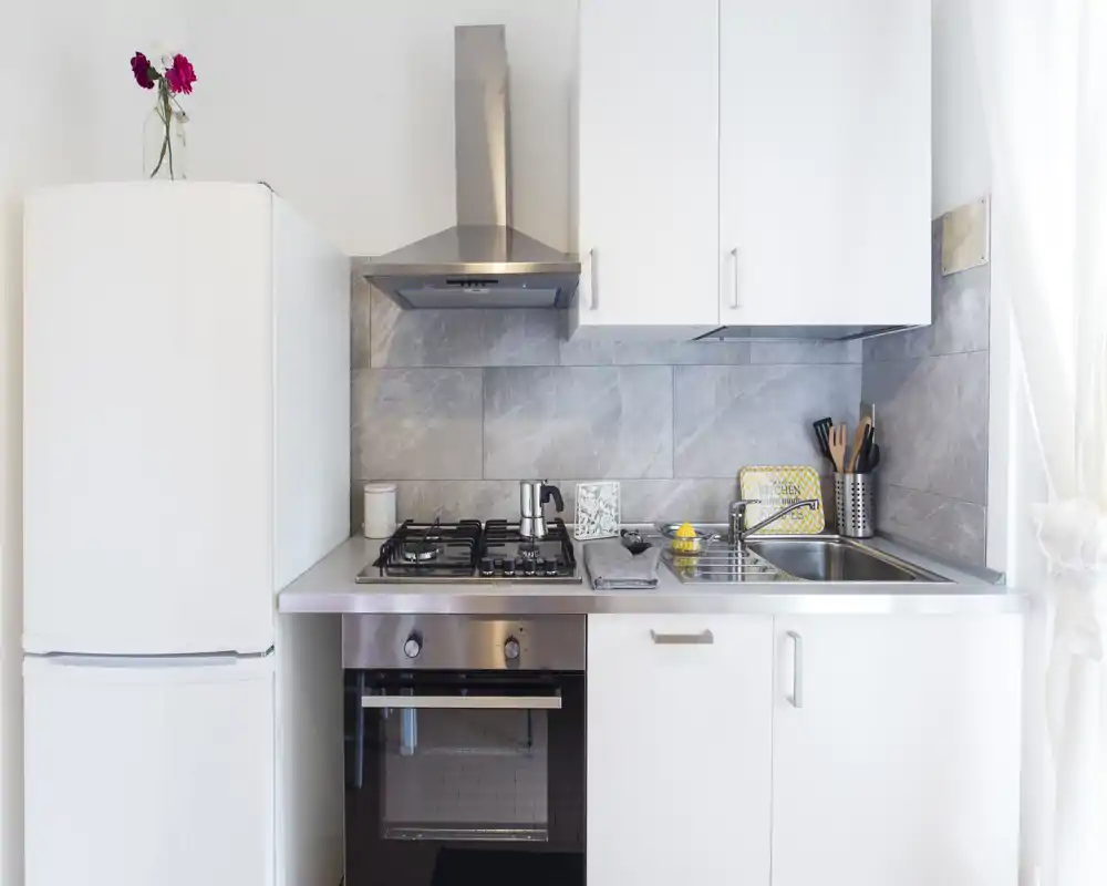 Cocina moderna y compacta con electrodomésticos de acero inoxidable, placa de gas, horno y fregadero; luminosa, limpia y bien organizada para alquileres de corta estancia.