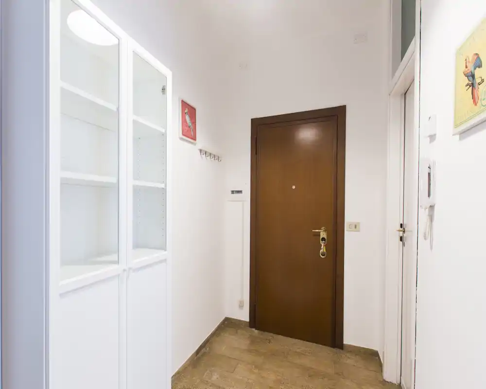 Vestíbulo luminoso y limpio con puerta principal de madera, suelo de baldosa y un armario blanco; ideal como zona de recibidor.