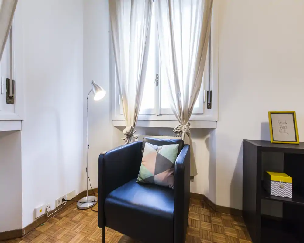 Rincón de salón acogedor con un sillón moderno, cojín decorativo y lámpara de pie junto a una ventana luminosa — ideal para leer o relajarse.
