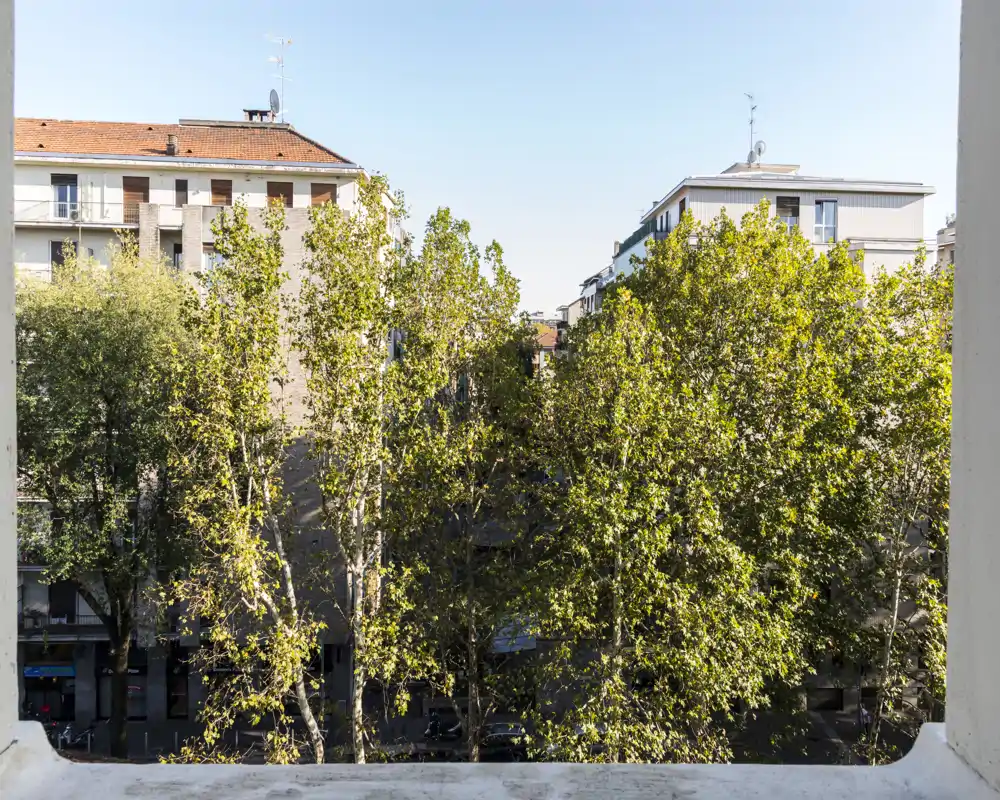 Balcony view overlooking treetops and neighbouring apartment buildings with clear daylight and blue sky — ideal to showcase an urban outdoor space.