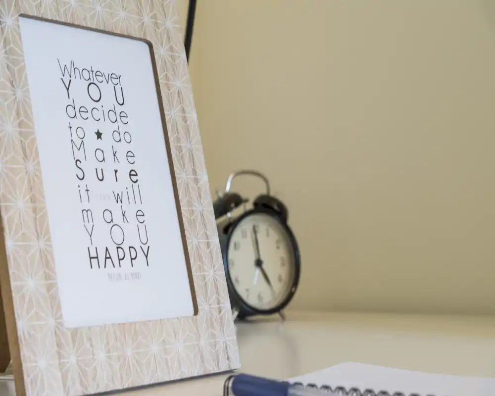 Close-up of a decorative frame and a classic alarm clock on a light surface; soft, neutral tones create a calm bedside or desk vignette.