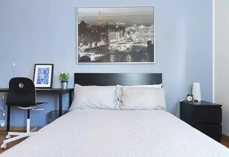 Camera da letto luminosa e curata con letto matrimoniale ben rifatto, comodino, scrivania e quadro decorativo; perfetta per annunci che puntano su comfort e design moderno.