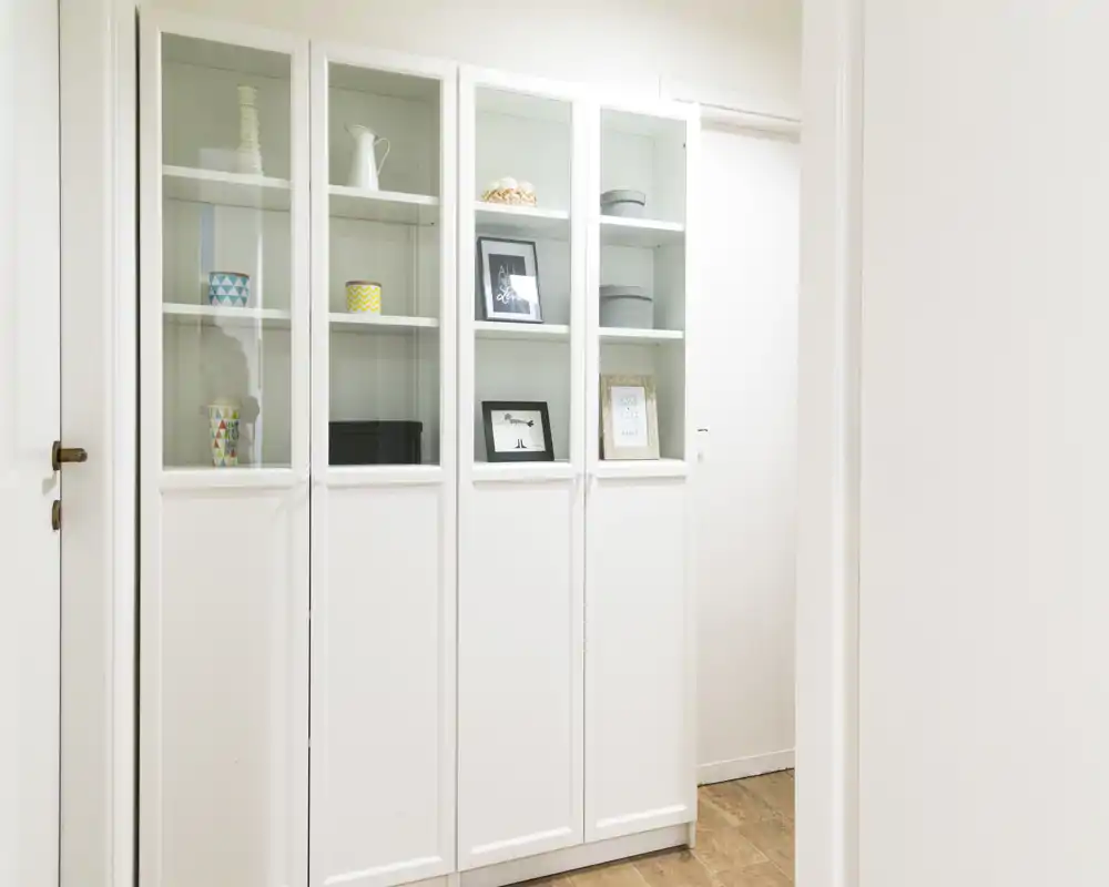 Ingresso/corridoio luminoso e minimal con un alto mobile bianco con ante in vetro superiori e oggetti decorativi.