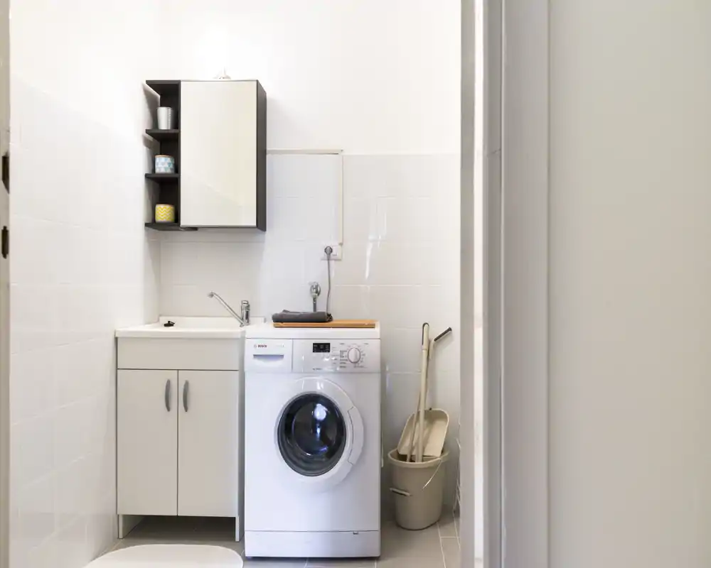 Angolo bagno/lavanderia luminoso e ordinato con lavatrice a carica frontale, mobile lavabo e pensile: spazio pratico per l'uso quotidiano.