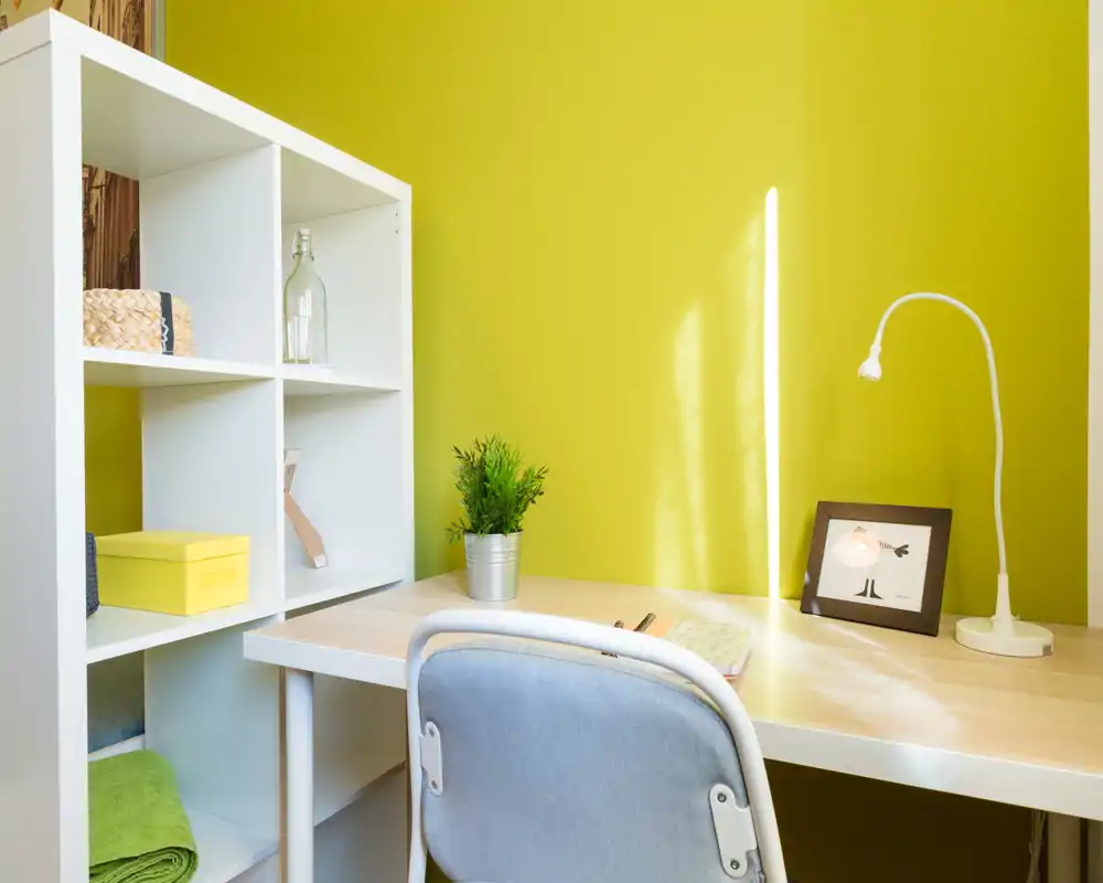 Rincón de estudio luminoso y ordenado con escritorio, lámpara, planta pequeña y estantería — ideal para trabajar o estudiar.
