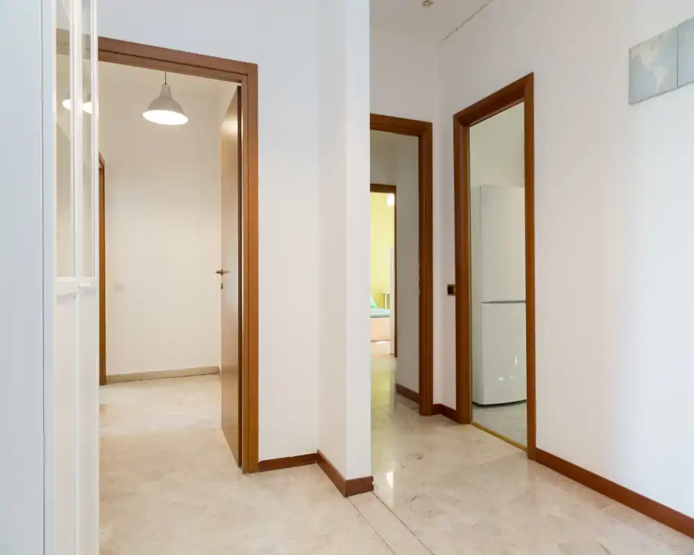 Entrada luminosa y limpia con varias puertas y suelo de mármol — ideal para mostrar la circulación y el acceso a las habitaciones contiguas.
