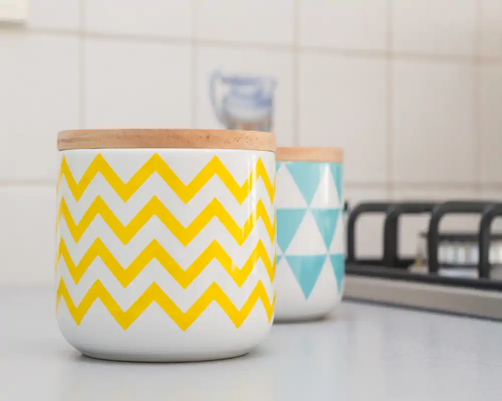 Primer plano de tarros decorativos en la encimera de la cocina junto a una placa de gas; azulejos modernos al fondo.
