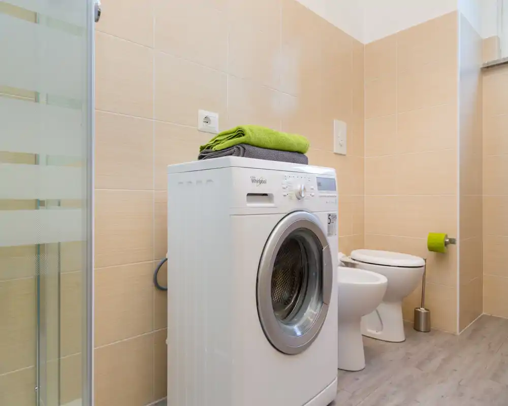 Baño moderno y limpio con lavadora, bidé e inodoro; azulejos neutros y luz natural que ofrecen una sensación práctica y fresca.