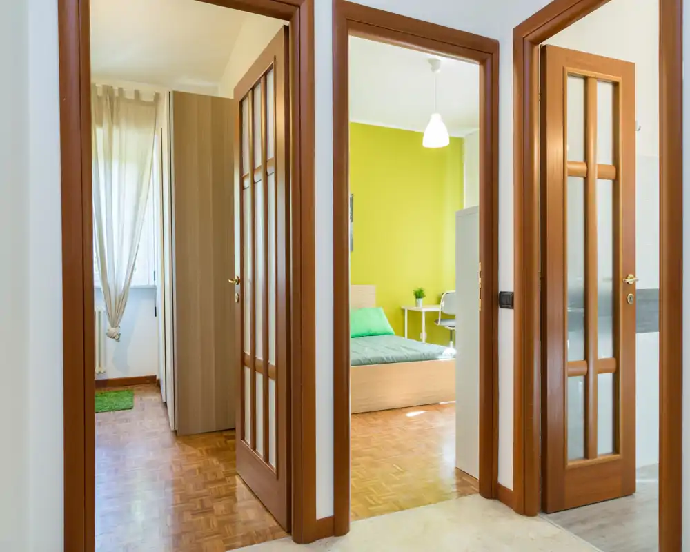 Dormitorio luminoso y bien presentado visto desde el pasillo, con pared verde, cama con cojines y mesita — ideal para un anuncio acogedor.