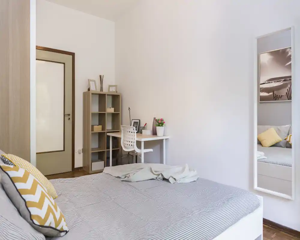 Bright, modern bedroom with a large visible bed, patterned cushions and a small workspace with shelving — airy, well-lit and tastefully styled for comfortable stays.