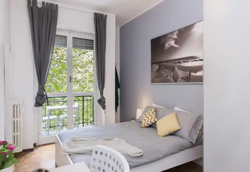 Bright, stylish bedroom with a double bed facing a balcony door, cozy textiles and tasteful wall art — ideal for a comfortable stay.