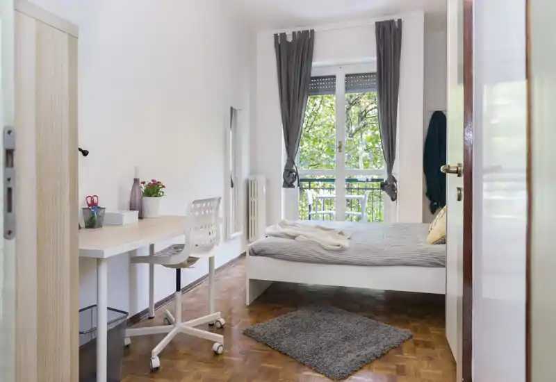 Bright, neat bedroom with a comfortable double bed, desk area and large window opening to greenery — ideal for relaxing and working.