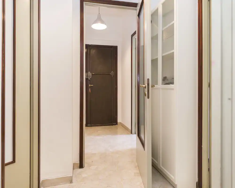 Bright, clean entrance hallway with a visible main door, tiled floor and built-in storage. Neutral walls and a pendant light create a welcoming first impression.