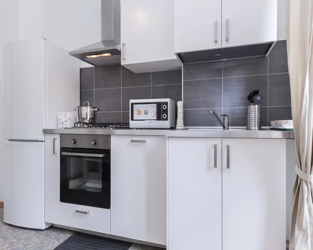 Compact modern kitchen with white cabinets, gas hob, built-in oven, microwave and fridge; bright, clean and well organized.