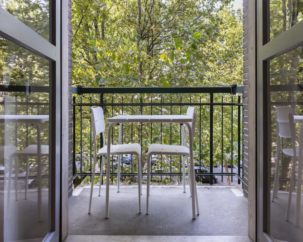 Sunny balcony with a small table and two chairs overlooking leafy trees — a quiet outdoor spot to relax or enjoy a coffee.