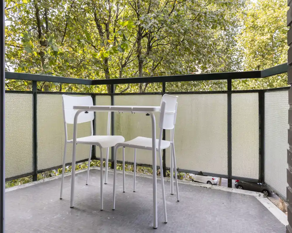 Sunny balcony with a small table and two chairs overlooking leafy trees — ideal for morning coffee or a quiet outdoor spot.