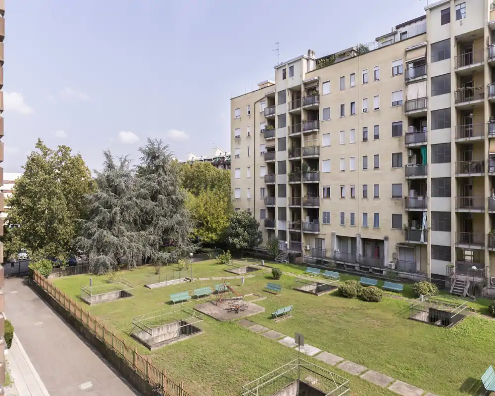 Sunny communal courtyard with grassy areas, benches and a central children’s play area, surrounded by residential buildings — ideal for outdoor relaxation.