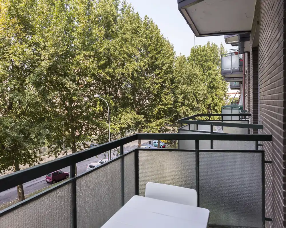 Sunny balcony with a small table and seating, overlooking tree-lined street — ideal for morning coffee and relaxed outdoor moments.