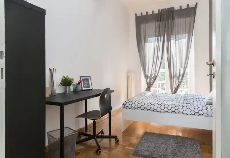 Chambre lumineuse et soignée avec lit double, bureau simple et lumière naturelle filtrée par un rideau — parfaite pour un séjour confortable.