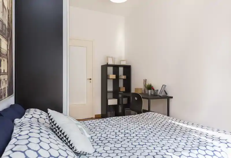 Chambre claire et décorée avec un grand lit à housse à motifs, un petit bureau et une étagère — agréable et accueillante.