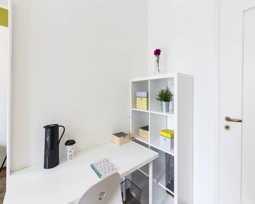 Coin bureau minimaliste et lumineux avec un bureau blanc, une étagère à cubes, une petite lampe et une plante décorative — idéal pour travailler ou étudier.