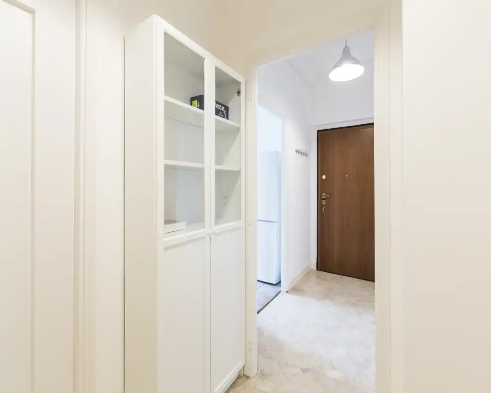 Entrée lumineuse et minimaliste avec un meuble de rangement blanc et une porte d'entrée en bois ; sol en marbre et suspension offrent une première impression soignée.