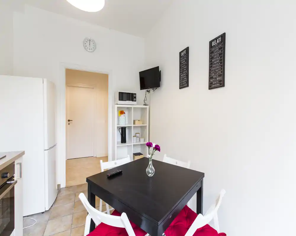 Coin repas compact et lumineux avec une table noire, quatre chaises blanches sur coussins rouges et un petit vase décoratif — idéal pour des repas informels en appartement.
