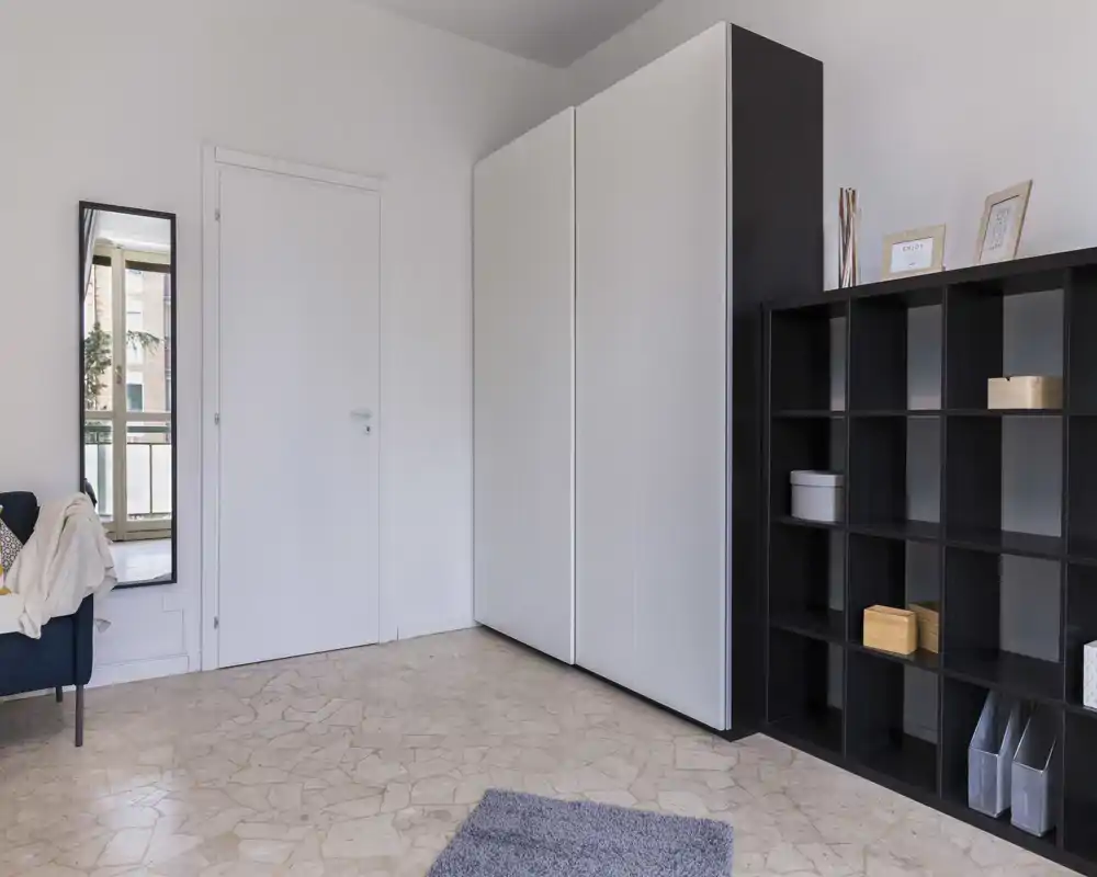 Espace de vie minimaliste et lumineux avec étagères modulaires et armoire ; décoration neutre avec un petit tapis et un miroir reflétant le balcon.