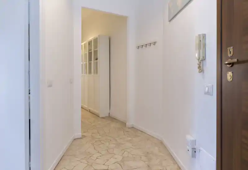 Entrée étroite et lumineuse avec sol carrelé, interphone mural et patères — espace d'accès propre et bien éclairé.