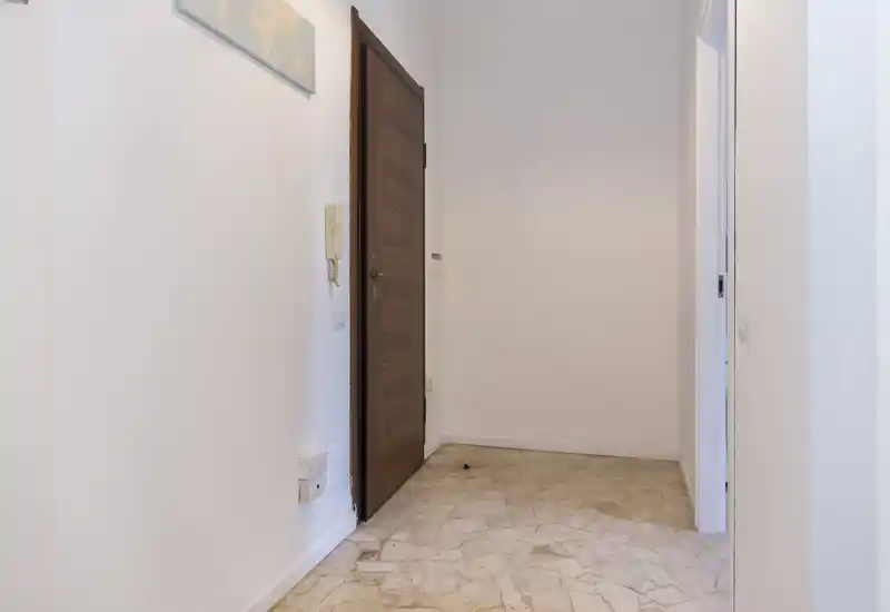 Entrée d'appartement lumineuse et propre avec porte d'entrée en bois, interphone et sol carrelé — un hall d'entrée neutre et bien éclairé.