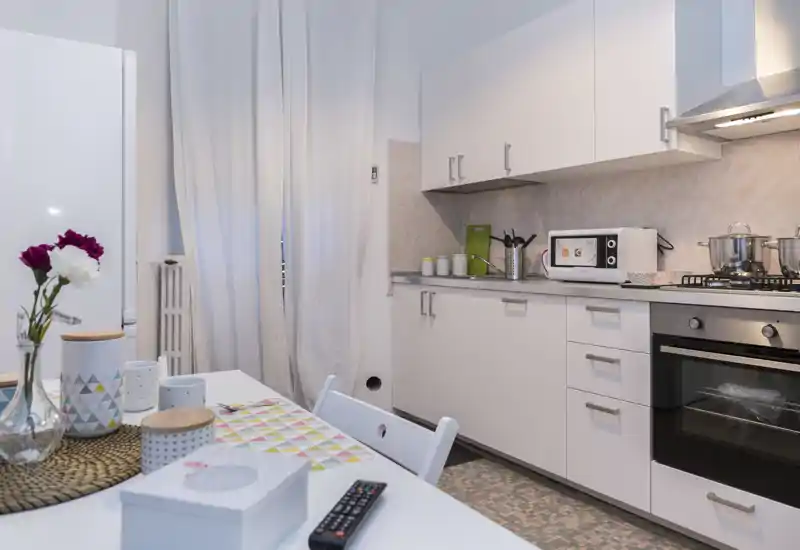 Cuisine moderne et lumineuse avec meubles blancs, plaque à gaz et micro-ondes ; une table décorée avec des fleurs apporte une touche chaleureuse.